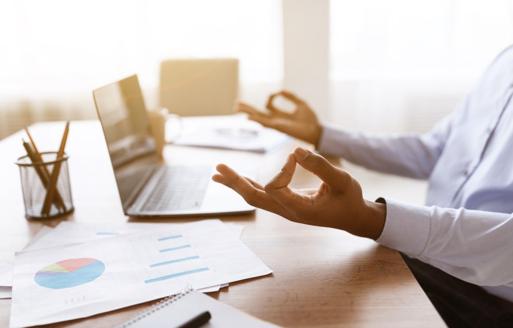 Cropped of unrecognizable black worker meditating while working in office, copy space. African american businessman trying to calm down during stressful period at work, closeup, sun flare