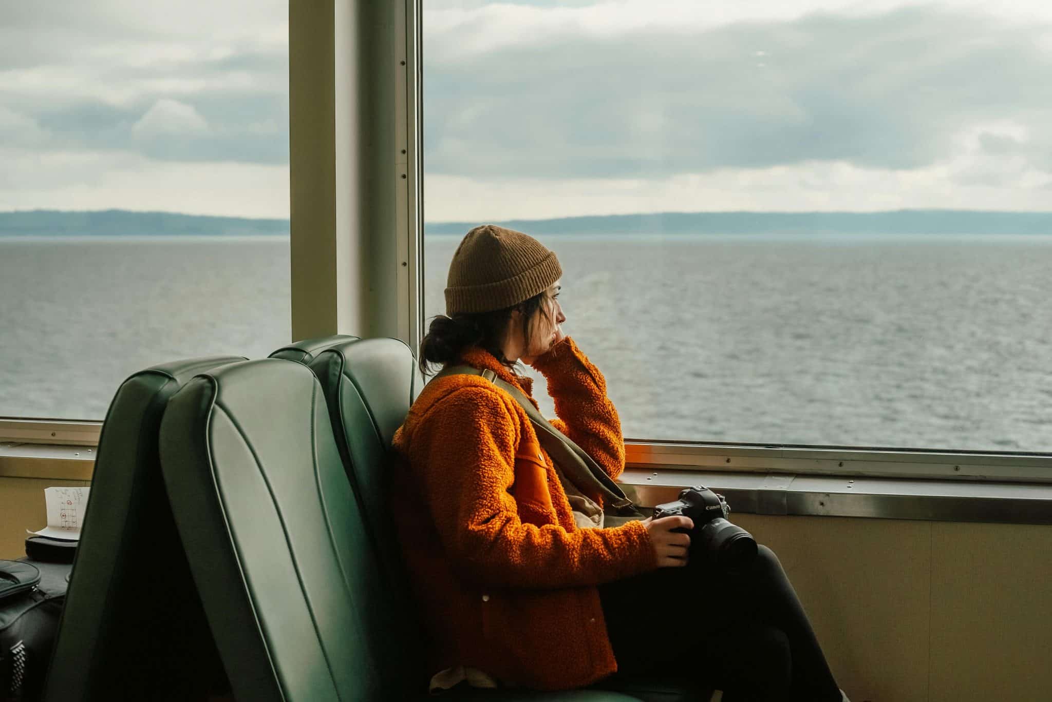 A woman gazes out the window of a train at the vast blue sea.