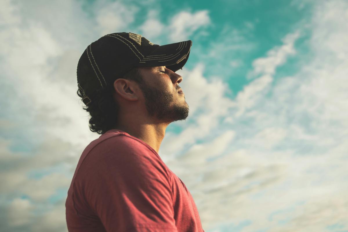 Man breathing in fresh air outdoors under a cloudy sky as part of a cortisol detox stress relief routine.