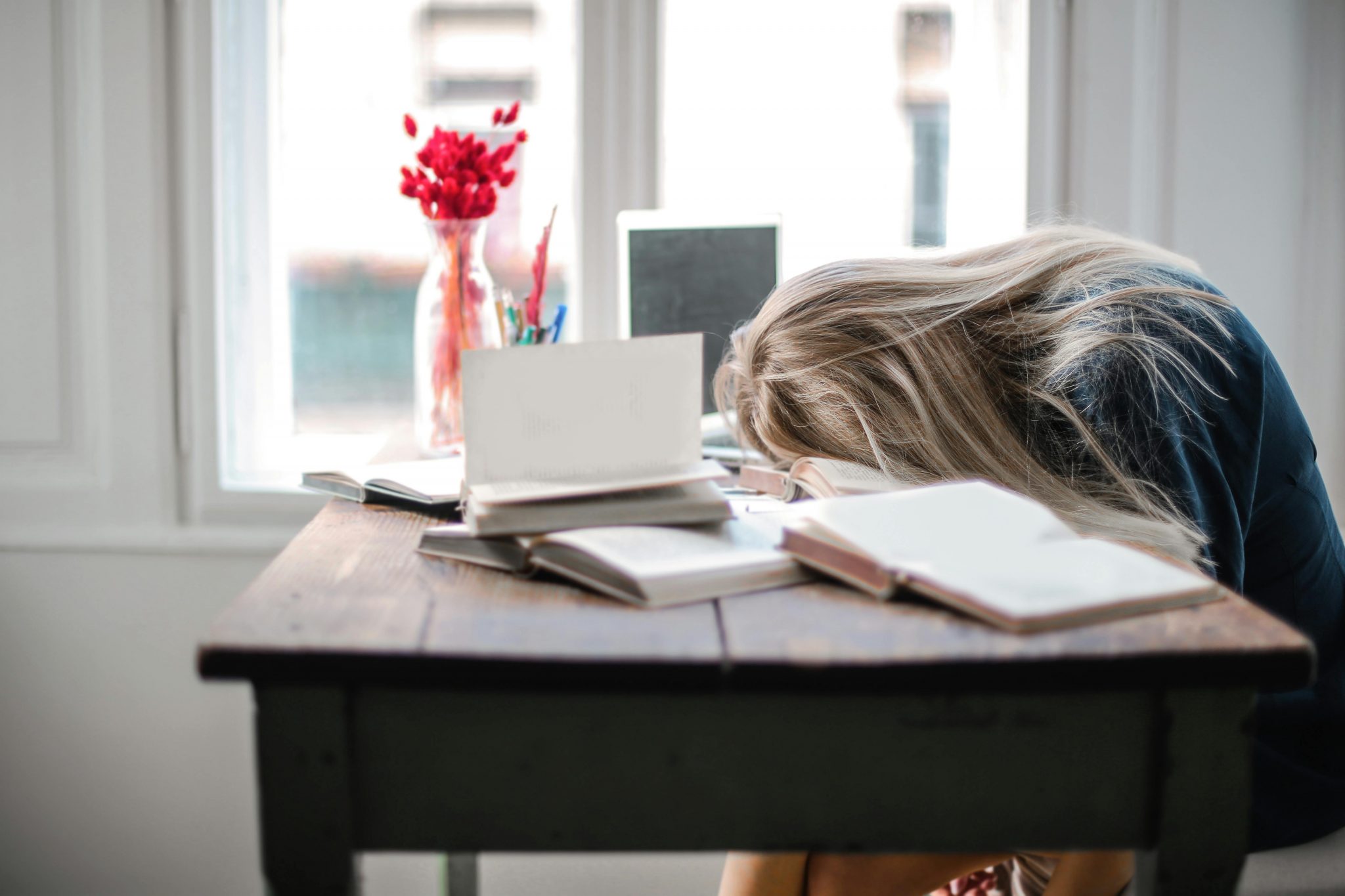 Stressed woman leaning on a desk with eyes closed, overwhelmed by work, representing high cortisol levels due to burnout and mental fatigue.