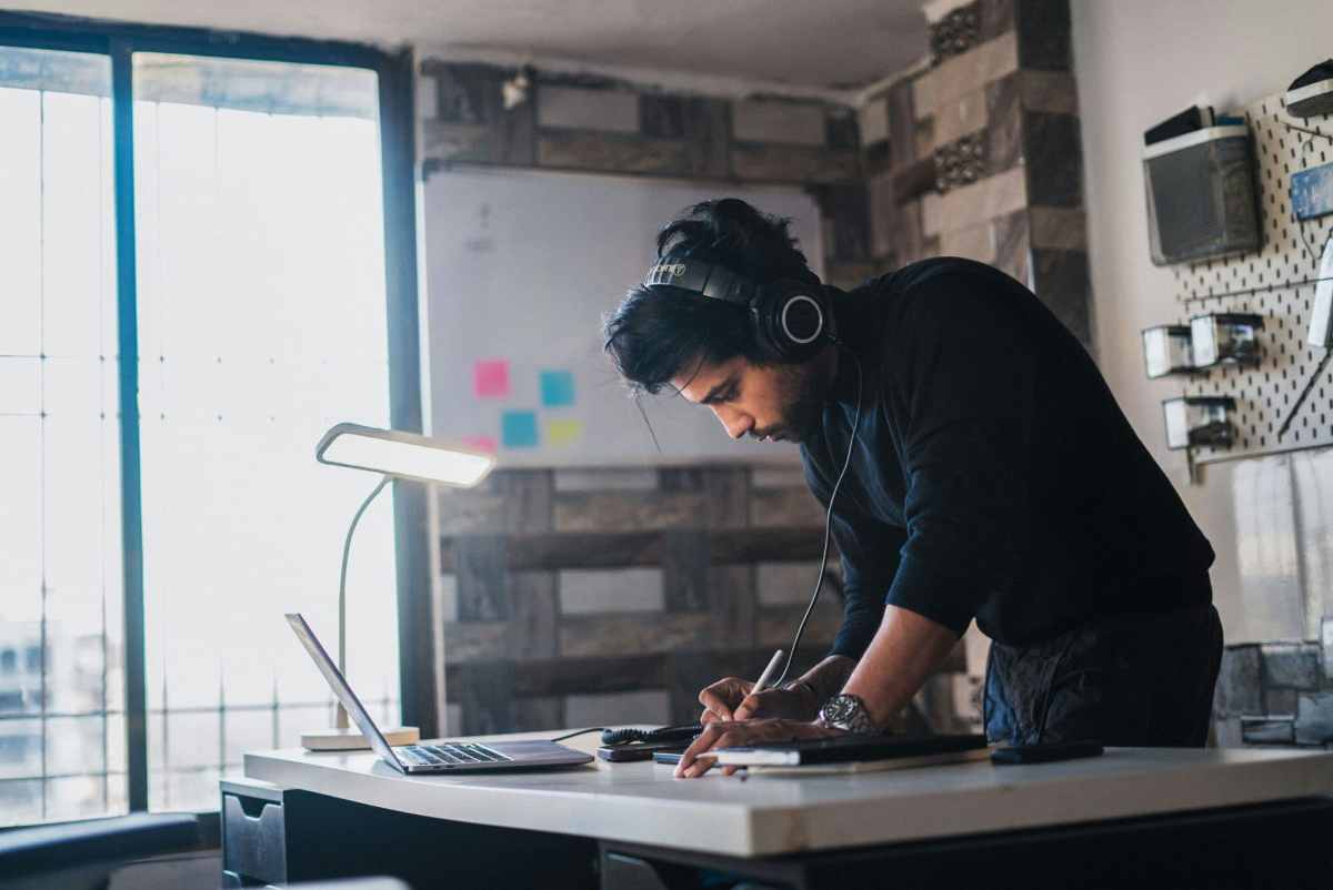 Man wearing headphones, locked in and focused at his desk, working intently on a laptop in a softly lit room.