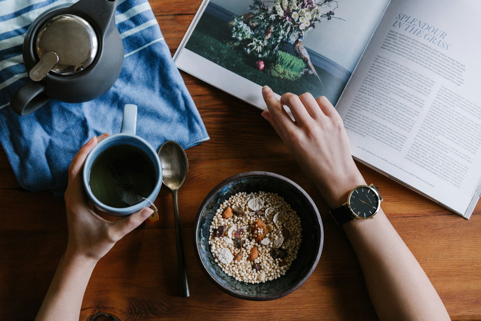 Person holding a blue ceramic mug and a magazine, enjoying a quiet moment as part of their daily routine.
